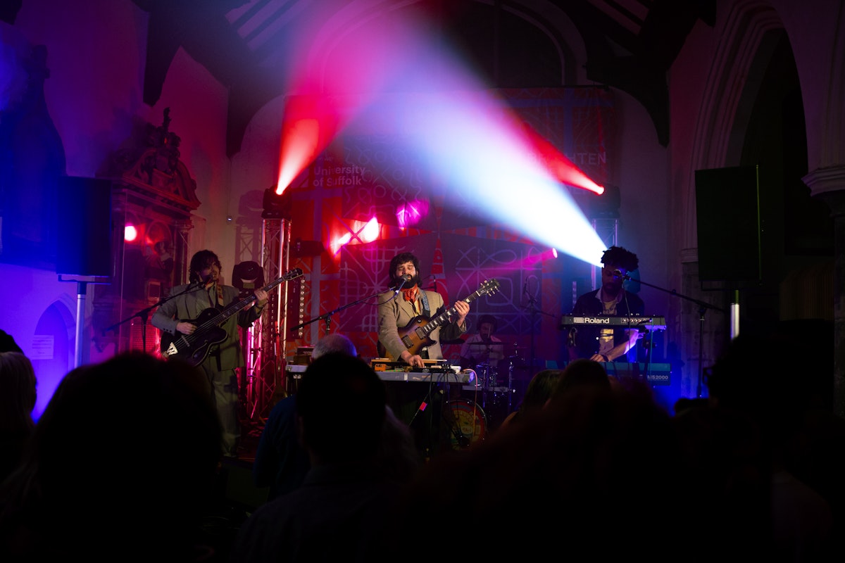 Flamingods performing on stage with dramatic pink and purple lighting, watched by a crowd inside St Stephen’s church venue